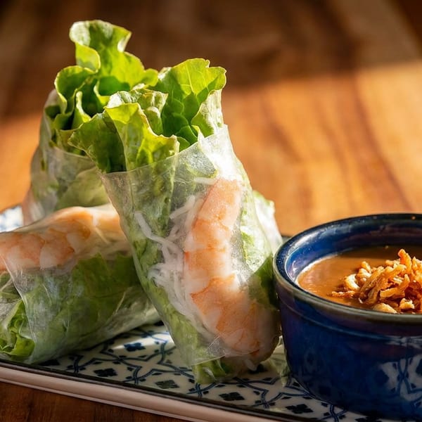 Three fresh spring rolls with shrimp and lettuce, served with peanut sauce on a patterned plate.