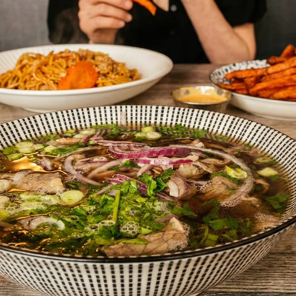 A bowl of pho with noodles, meat, and herbs, alongside sweet potato fries and noodles.