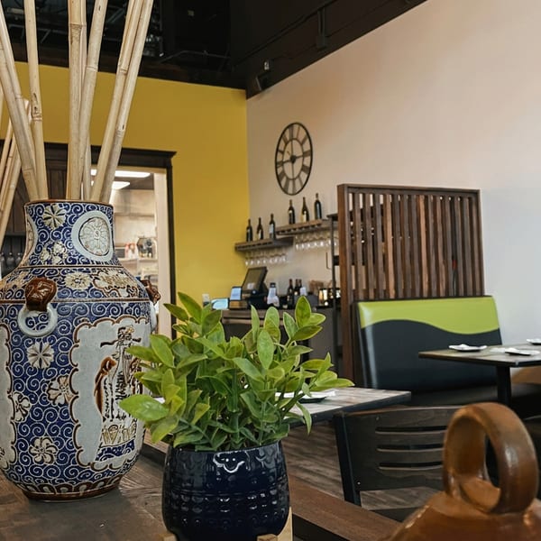 Restaurant interior with decorative vases, green plants, booths, and Asian string instruments on a white wall.
