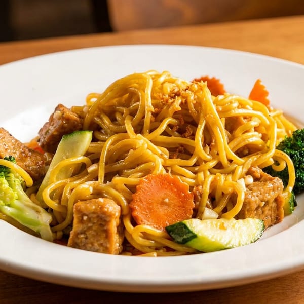 Noodle dish with tofu, broccoli, carrots, and zucchini on a white plate.
