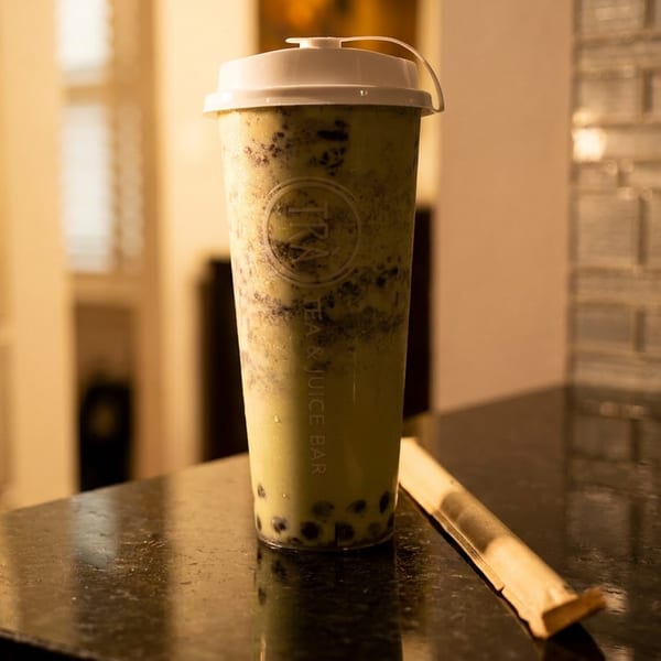 A tall plastic cup of bubble tea with dark boba pearls sits on a dark countertop.