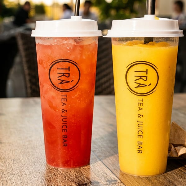 Two Tra Tea & Juice Bar drinks, one red and one yellow, on a wooden table.